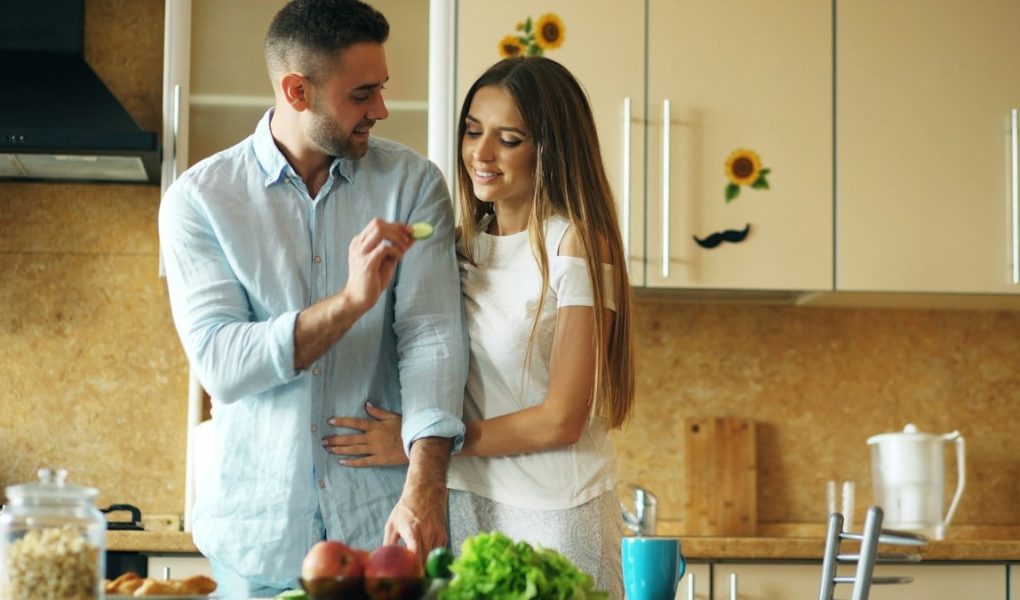 Happy young couple in the kitchen. Handsome man meet and feed his girlfriend early morning at home