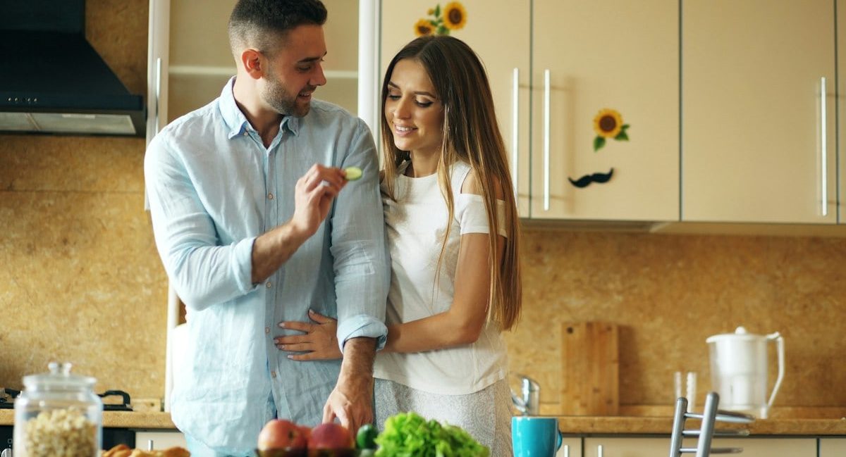 Happy young couple in the kitchen. Handsome man meet and feed his girlfriend early morning at home