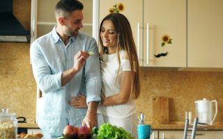 Happy young couple in the kitchen. Handsome man meet and feed his girlfriend early morning at home
