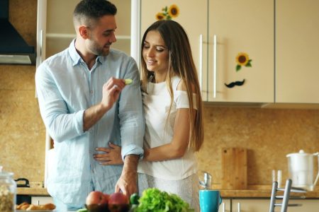 Happy young couple in the kitchen. Handsome man meet and feed his girlfriend early morning at home