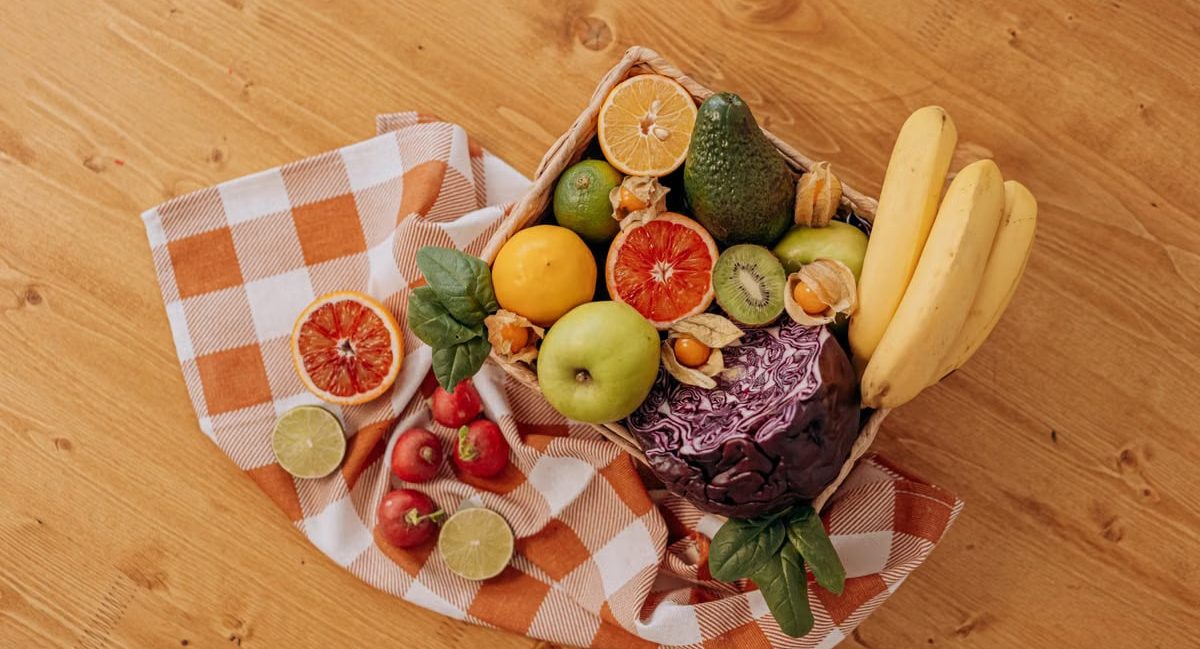 A vibrant flat lay of assorted fresh fruits on a checkered cloth over a wooden surface, perfect for healthy lifestyle concepts.